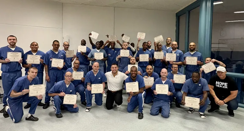 Men in blue prison uniforms holding up certificates of baptism