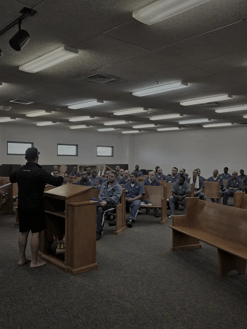 Frank Ortega teaching from a pulpit inside a Florida prison chapel filled with inmates in blue uniforms